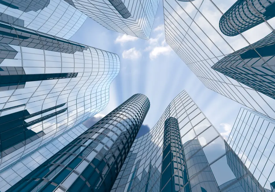 Low angle view of several modern blue glass skyscrapers reaching toward a bright blue sky with light clouds.