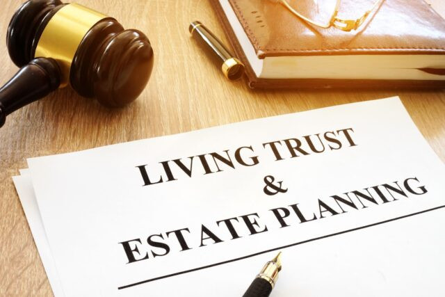 A document labeled "Living Trust & Estate Planning" on a desk with a gavel, eyeglasses, pen, and a closed book.