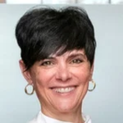 A woman with short dark hair and hoop earrings smiles at the camera against a light background.